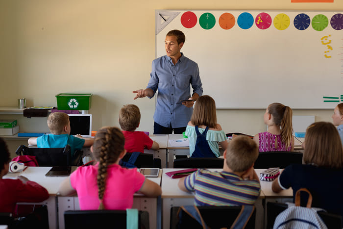 male school teacher standing in an elementary scho GRTFQMA 1